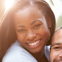 Smiling Black woman embracing someone, bathed in sunlight.